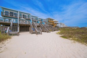 Ein Strandhotel mit mehreren Etagen, Sitzgelegenheiten im Freien und einer Holztreppe zum Strand.