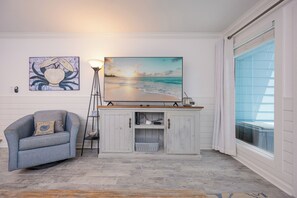 Ein Zimmer mit Blick auf den Strand, ein blauer Sessel, eine weiße Kommode und ein Bild von einem Krabben.