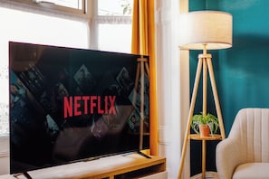A television with the Netflix logo, a lamp, and a potted plant in a room with teal walls. - Central Stadium House | Free Parking | 15PPL (Sheffield)