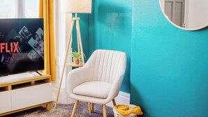 Un salon avec un téléviseur affichant le mot « FLIX », un fauteuil blanc, une lampe sur pied et un mur bleu.