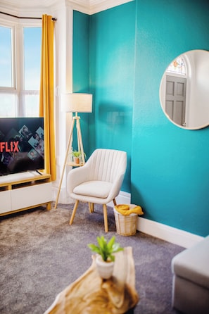 A living room with a television displaying the word 'FLIX,' a white chair, a floor lamp, and a blue wall. - Central Stadium House | Free Parking | 15PPL (Sheffield)