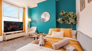 Une chambre d’hôtel avec un lit, un téléviseur affichant le logo « NETFLIX », une chaise, une plante et une fenêtre.