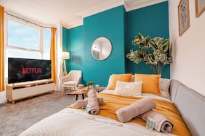 A hotel room with a bed, a TV displaying 'NETFLIX,' a chair, a plant, and a window. - Central Stadium House | Free Parking | 15PPL (Sheffield)