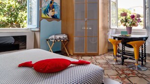 A bedroom with a bed, a red pillow, a wardrobe, a table with yellow chairs, and a window with a view of greenery. - Bed and Breakfast 'Sentieri' with Wi-Fi and Air Conditioning (Levanto)