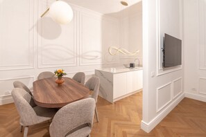 A dining area with a round table, six chairs, a vase with flowers, a kitchen with a marble countertop, and a TV mounted on the wall. - Located on elegant Via Tacito in the prestigious Prati district, this stunning designer apartment offers a unique stay in the heart of Rome. Spacious and bright, it features three bedrooms, three refined bathrooms, a stylish living area and a modern kitc (roma)
