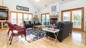 A spacious living room with a fireplace, large windows, and a high ceiling. - Ocean View from Balconies | Steps to Private Beach (Rehoboth Beach)