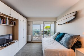 Um quarto moderno com televisão, sofá, estante de livros e porta de vidro deslizante para uma varanda.