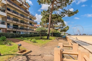 A multi-story building with balconies, a pathway, a tree, and a Ferris wheel in the background. - Studio Sea View Apartment – Direct Beach Access, Private Terrace, Wi-Fi (Arcachon)