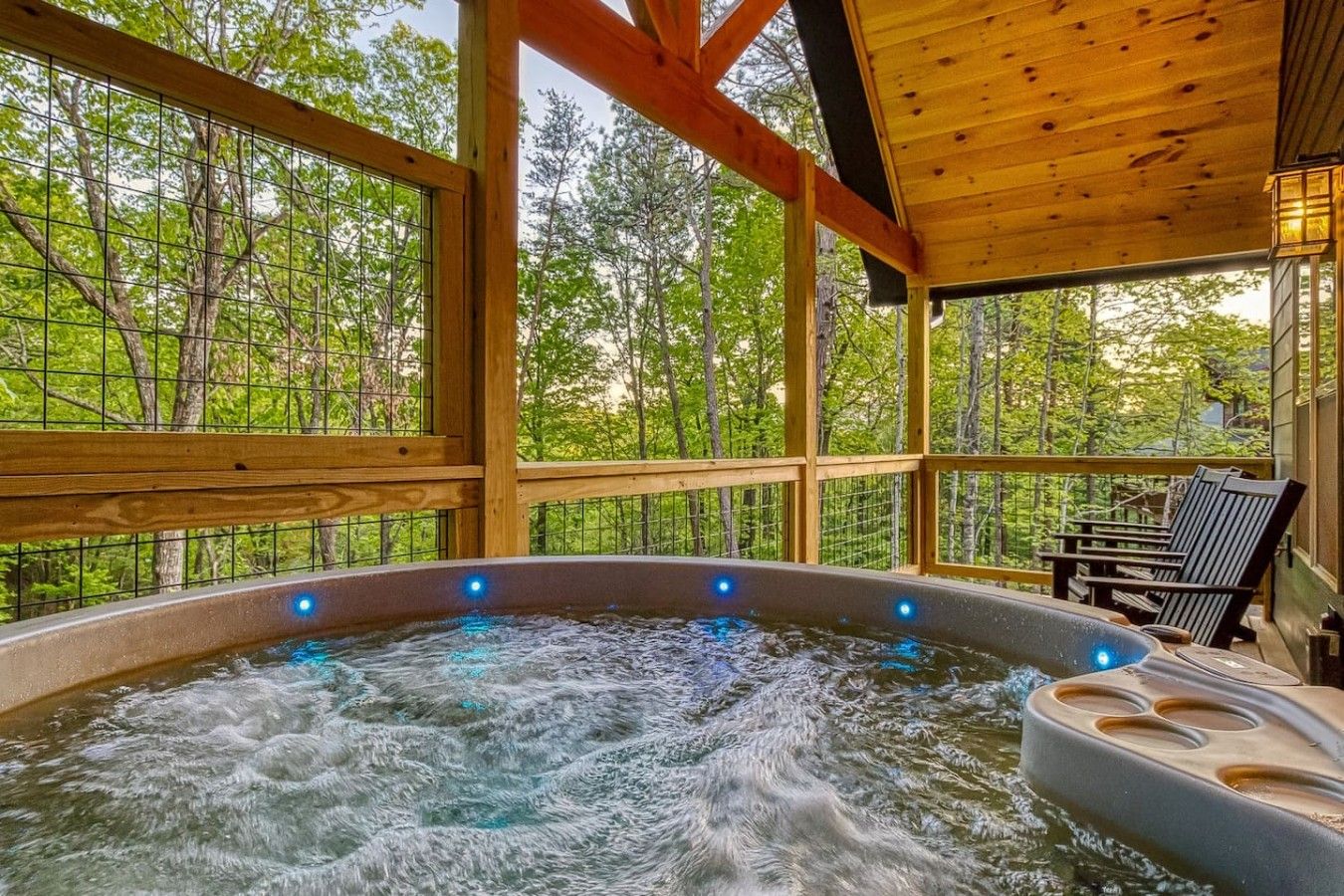 A hot tub with a wooden deck and chairs, surrounded by trees.