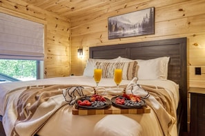 A wooden cabin bedroom with a bed, two bedside tables, a nightstand, a window, and a framed picture on the wall. - Twilight Escape | Designer Cabin + Firepit & Views (Sevierville)
