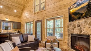 A log cabin interior with a stone fireplace, leather sofas, and a dining area. - Twilight Escape | Designer Cabin + Firepit & Views (Sevierville)