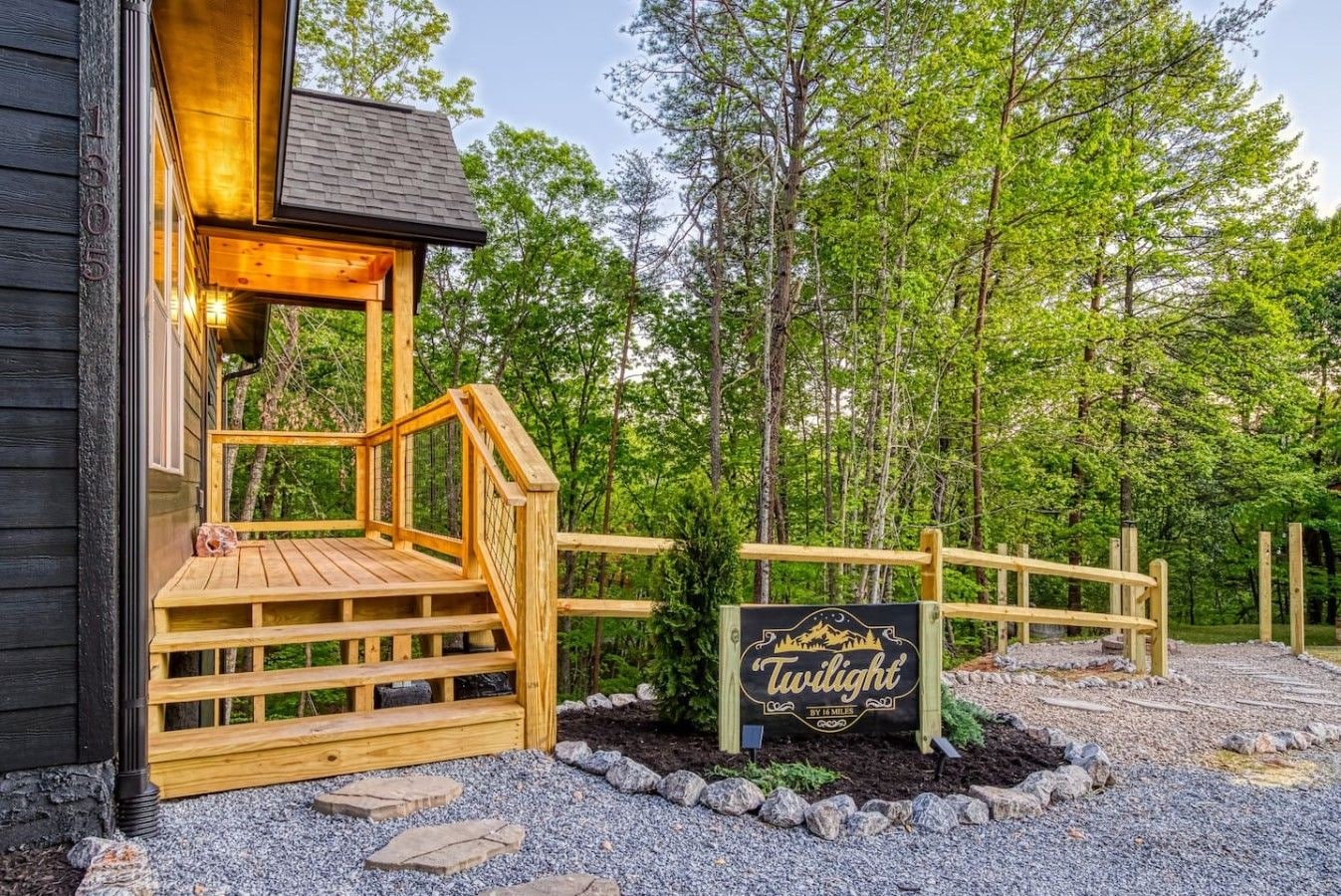 A wooden deck with a staircase leading to a building entrance, surrounded by a forested area.