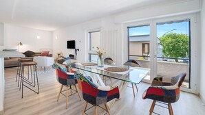 Un salon moderne avec une table à manger en verre, des chaises colorées, un canapé et un téléviseur.