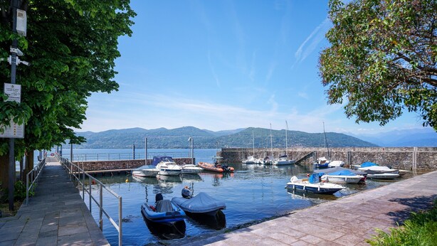 Un port de plaisance avec des bateaux amarrés, un sentier pavé de pierres et une vue sur des collines lointaines.