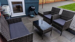 A patio with wicker furniture, a grill, and a window. - Luxury 2 bed house (Bristol)