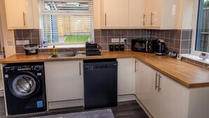 A compact kitchen with a washing machine, dishwasher, microwave, and a coffee maker. - Luxury 2 bed house (Bristol)