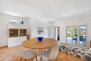 Ein Essbereich mit einem runden Holztisch, weißen Stühlen, einer blauen Schüssel und einem weißen Schrank mit Glastüren.