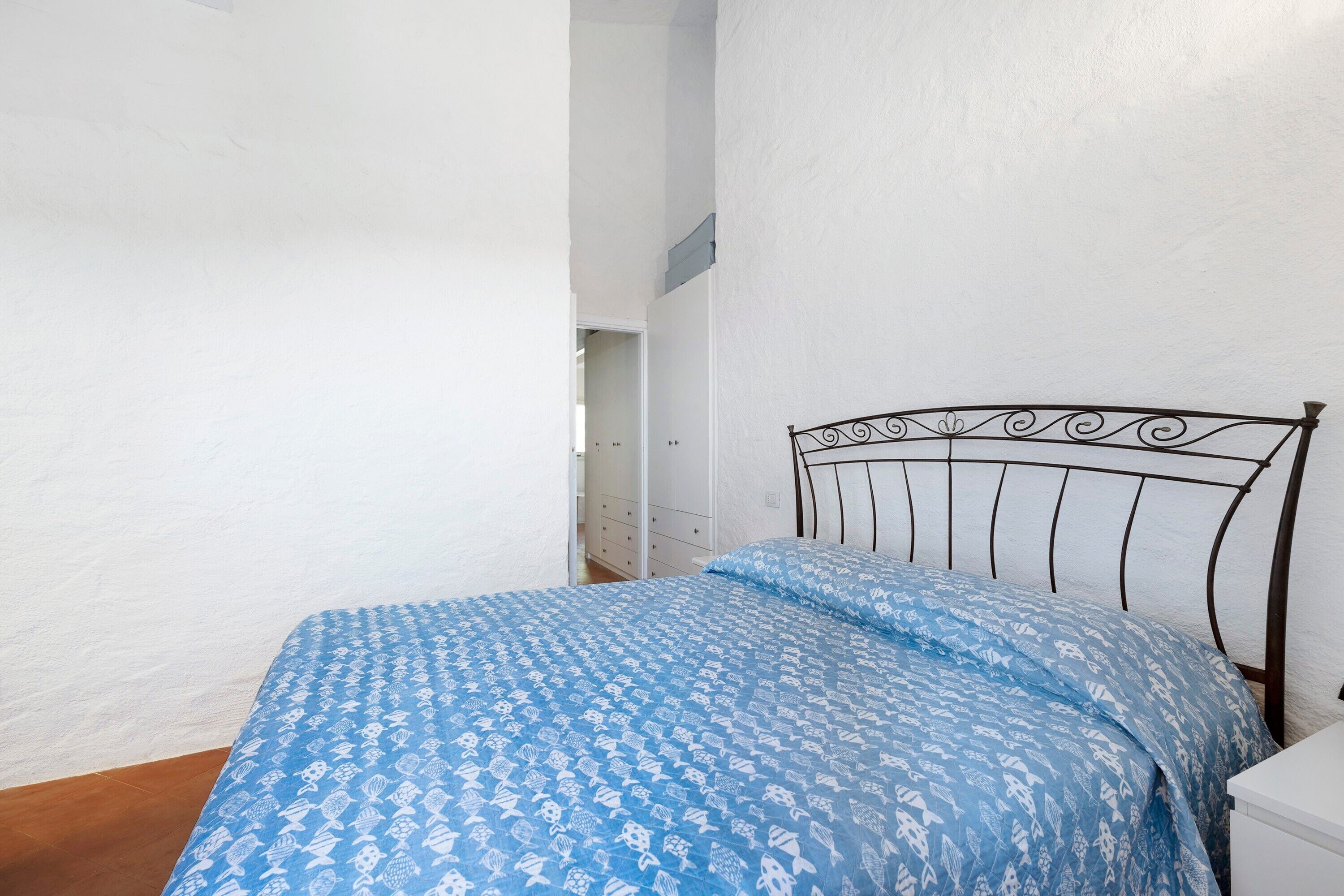 Un dormitorio con cama, paredes blancas y suelo de madera.