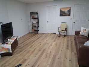 A living room with a wooden floor, a TV on a stand, a bookshelf, a chair, and a couch. - Whispering Pines is a lovely 3-bedroom family-friendly home in a wooded setting. (New Pekin)