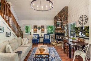 A living room with a fireplace, wooden staircase, and a stone wall. - Creekside Retreat | Hot Tub Bliss & Firepit Nights (Ellijay)