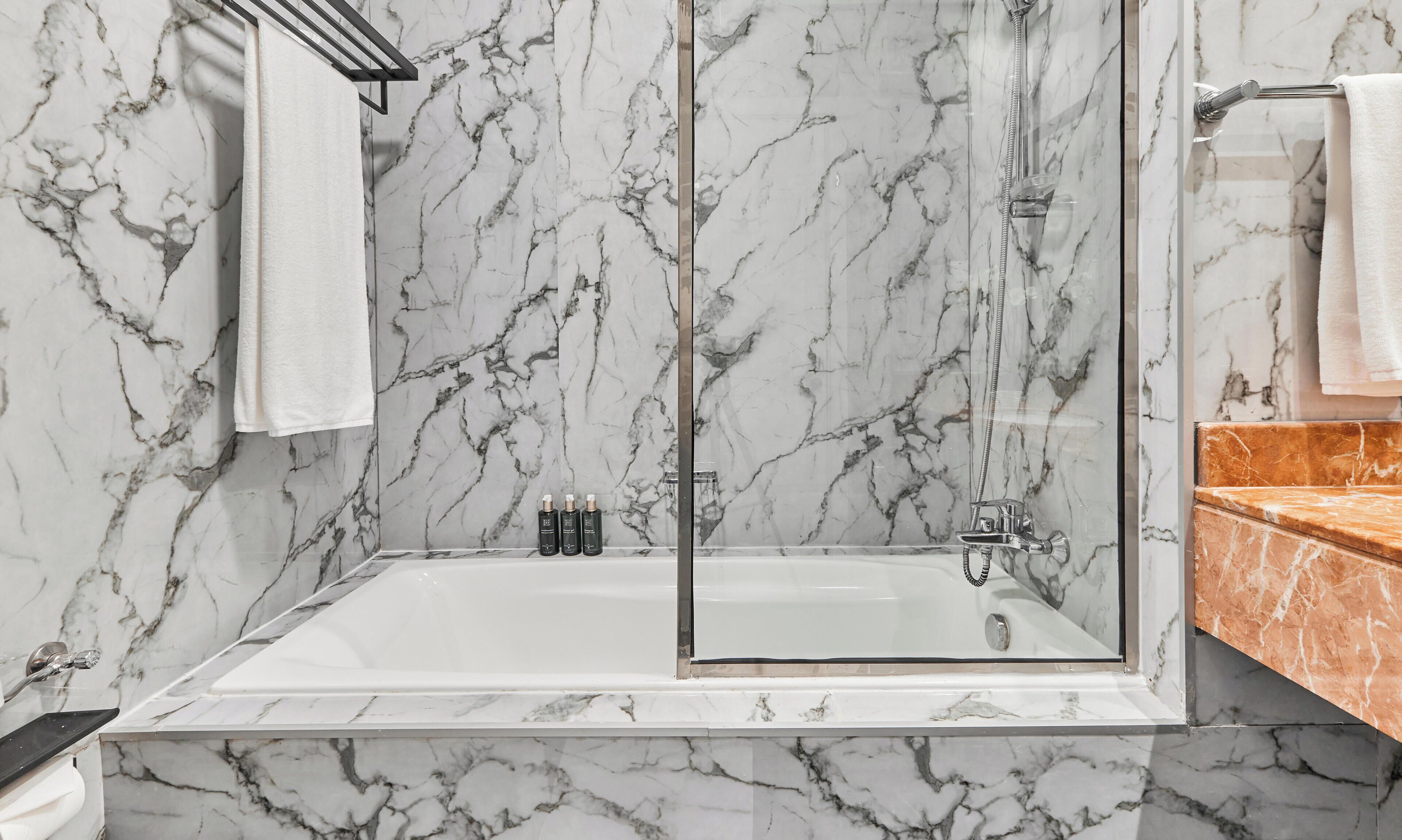 Une salle de bain avec un mur en marbre, une baignoire, une douche et un meuble-lavabo doté d’un plan de toilette en marbre.