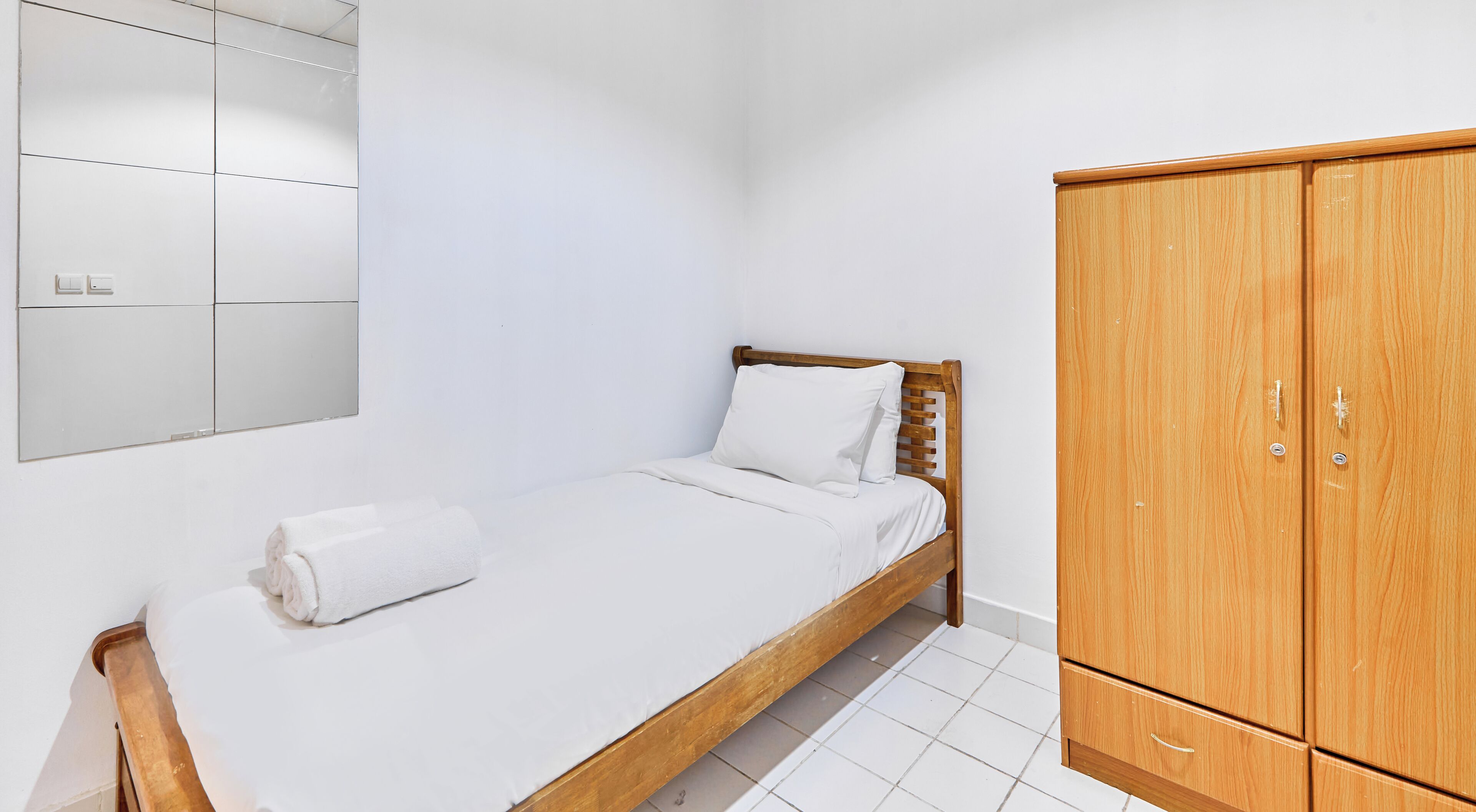 A single bed with a wooden headboard, a wooden wardrobe with two doors, and a wall-mounted mirror.
