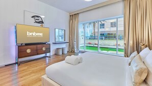 A hotel room with a large bed, a television, a window with a view of a pool, and a 'bnbme' sign. - bnbme - Emirates Crown - 2BR & Maid Room (Dubai)