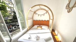 Una cama individual con cabecera de madera, ropa de cama blanca y vista a la calle a través de una ventana.