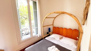Una cama individual con cabecera de madera, una ventana con persianas y una mesita de noche con lámpara.