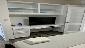 Ein Schlafzimmer mit Bett, Fernseher, Kleiderschrank und Schreibtisch mit Schubladen.