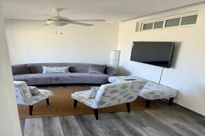 A living room with a grey sofa, two patterned armchairs, a brown rug, a ceiling fan, and a mounted TV. - Cap Cana - Cozy 2BR: Pools, Beaches, Marina & Golf (Punta Cana)