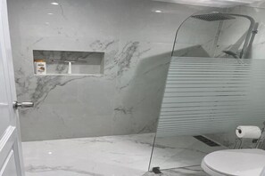 A modern bathroom with a glass-enclosed shower, marble walls, and a toilet. - Cap Cana - Cozy 2BR: Pools, Beaches, Marina & Golf (Punta Cana)