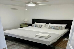 A bedroom with a bed, a nightstand, a lamp, and a ceiling fan. - Cap Cana - Cozy 2BR: Pools, Beaches, Marina & Golf (Punta Cana)