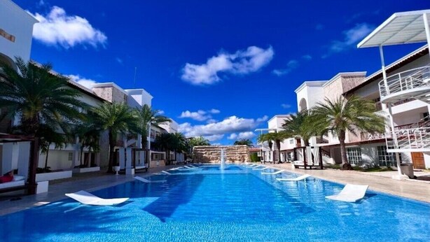 Ein Pool mit Liegestühlen, Palmen und blauem Himmel.