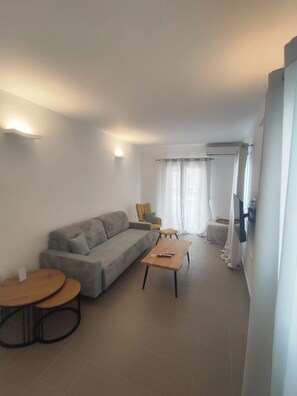 Ein modernes Wohnzimmer mit einem grauen Sofa, einem Holztisch, einem gelben Sessel und einem kleinen runden Tisch.