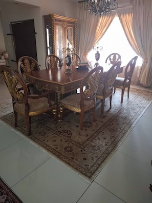 Un comedor con una mesa de madera y sillas ornamentadas, un espejo grande y una araña.