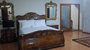 A bedroom with a wooden bed, two ornate mirrors, a ceiling fan, and a nightstand with a television. - The Address Luxurious (Johannesburg)