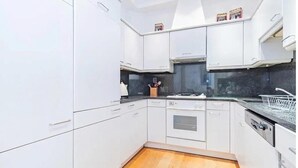 Moderni keittiö, jossa on valkoiset kaapit, musta työtaso ja puulattia.