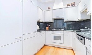 A modern kitchen with white cabinets, a black countertop, and a wooden floor. - Premium Central London Stay Near Sloane Square (London)