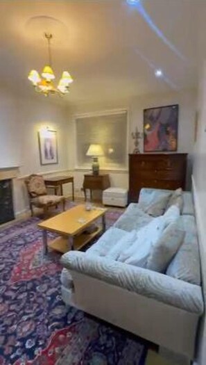Ein Wohnzimmer mit Sofa, Couchtisch, Lampe, Kamin und einem großen Fenster.