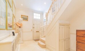 A hallway with a marble floor, a bust sculpture, a staircase, and a wooden dresser. - Premium Central London Stay Near Sloane Square (London)