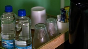 Una estantería con botellas de agua, un recipiente blanco y un objeto negro.