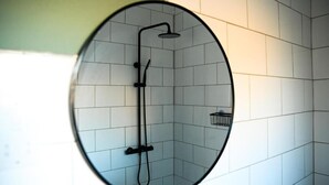 Espejo circular que refleja una zona de ducha con azulejos blancos y una ducha negra.
