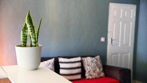 Una sala de estar con una mesa blanca, una planta en maceta, un sofá rojo y una puerta al fondo.