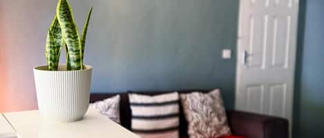 Un salon avec une table blanche, une plante en pot, un canapé rouge et une porte visible au fond.