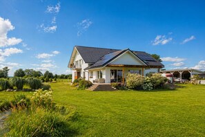 Una casa de dos pisos con techo inclinado, paneles solares, un porche cubierto y un césped cuidado.