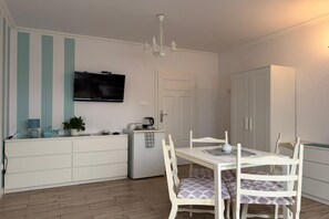 Una cocina moderna con comedor, armarios blancos, televisor de pantalla plana y candelabro.