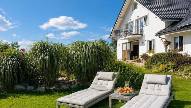 A house with two sun loungers in the garden, a balcony, and a clear blue sky. - Agritourism, family studio. (Ładzin)