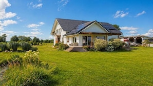 A house with a sloped roof, solar panels, a covered porch, and a well-maintained lawn. - Agritourism, family studio. (Ładzin)