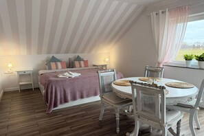 A bedroom with a bed, bedside tables, a dining table with chairs, and a window with a view. - Agritourism, family studio. (Ładzin)